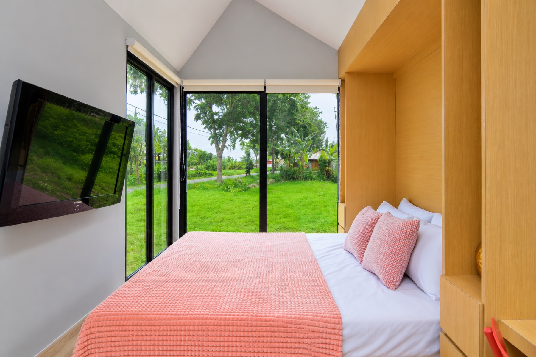 Caseea cabin interior — vaulted ceiling, queen bed with pink throw, full-height windows overlooking lush greenery.