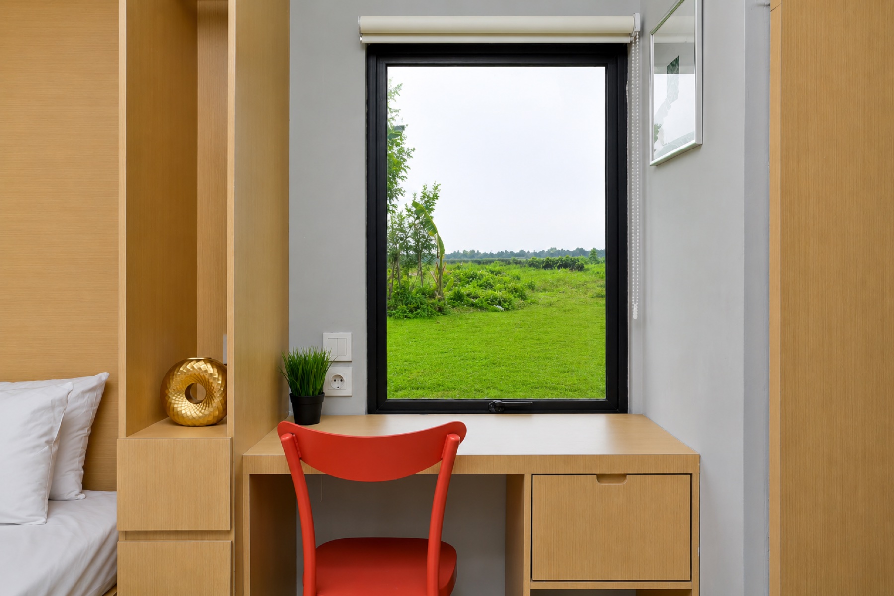 Caseea cabin interior — built-in oak desk and orange chair beside a large window with a view of rice fields.