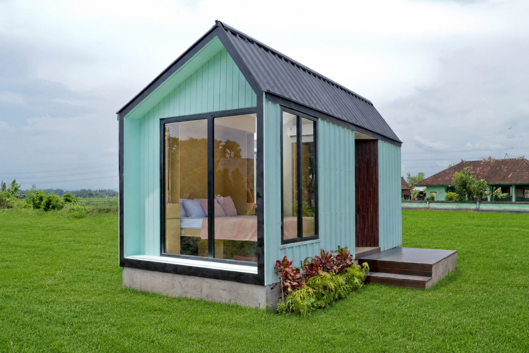 Caseea mint-green prefab cabin set on a Balinese rice paddy under a soft cloudy sky.